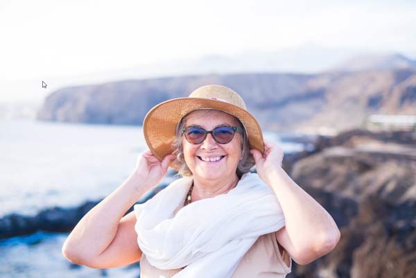 En kvinna som bär hatt och solglasögon njuter av solskenet och har fått en resa som pensionärspresent